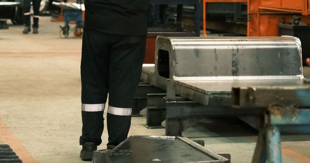 Metal imalat atölyesinde kaynaklı çelik parçalar ve çalışan
